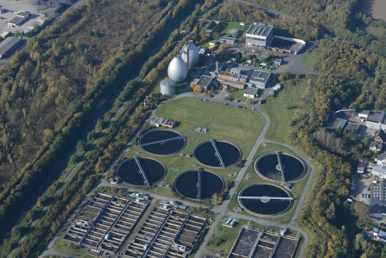 Vue aérienne d'une station d'épuration : bassins circulaires de décantation et digesteurs en forme d'œuf, entourés de bois.